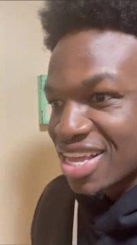 a young man with an afro smiles in front of a camera